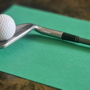 Golf ball balancing on iron club over green surface