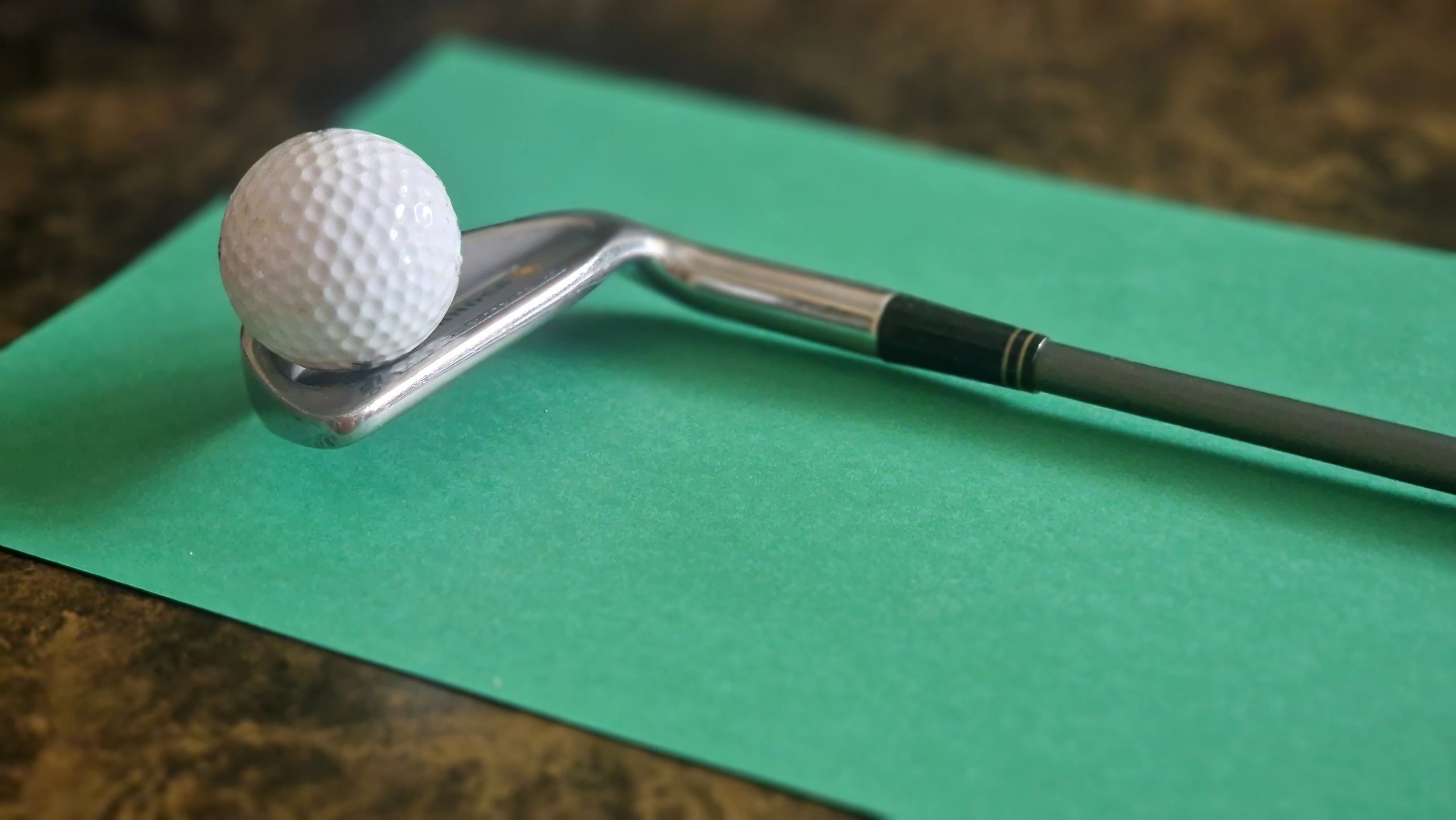 Golf ball balancing on iron club over green surface